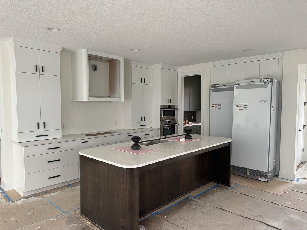 Near-complete luxury kitchen with white cabinetry dark wood island and quartz countertops in McDonald Construction home
