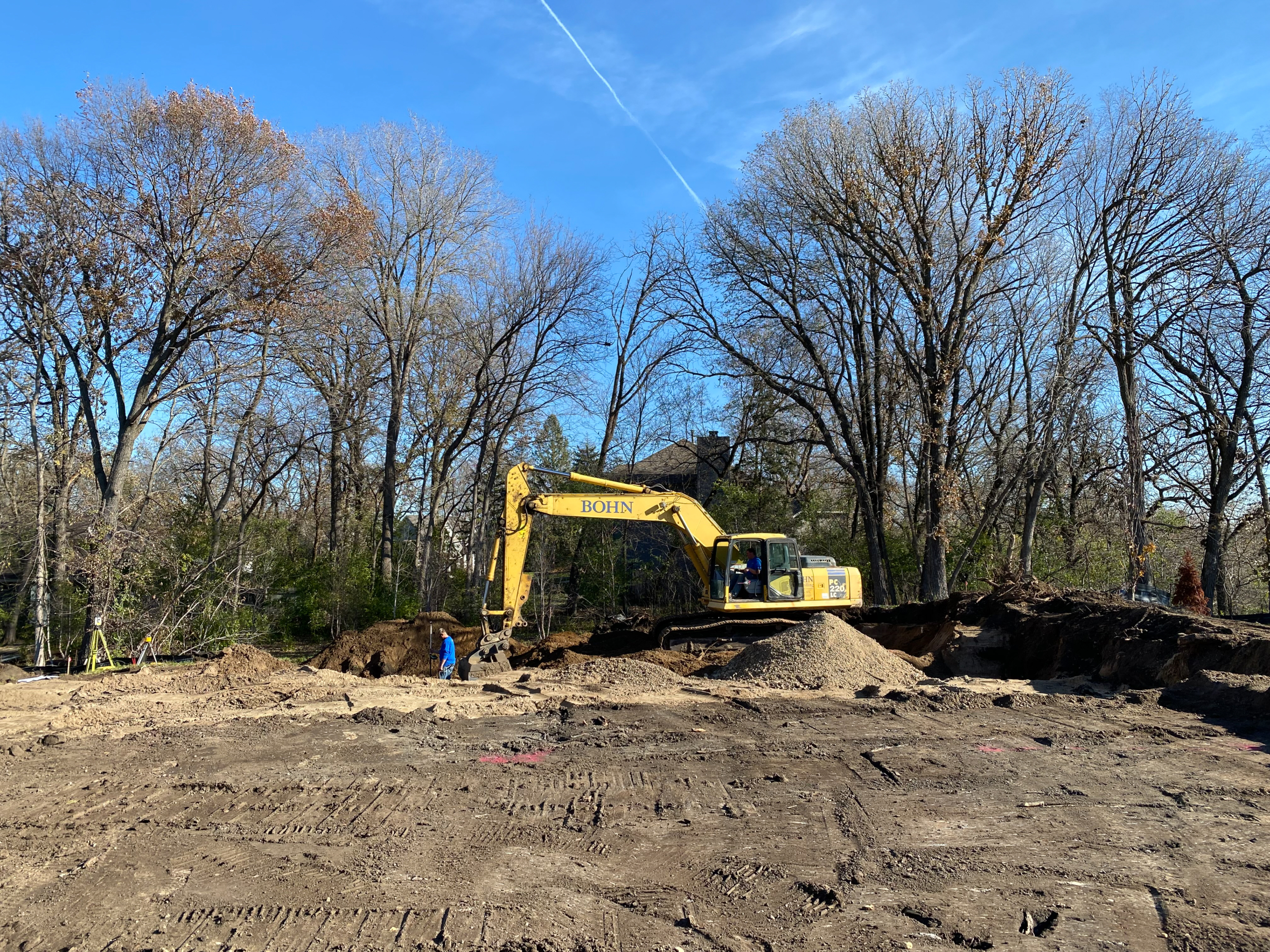 Bohn excavator breaking ground on wooded homesite during excavation and foundation phase of new construction custom home build