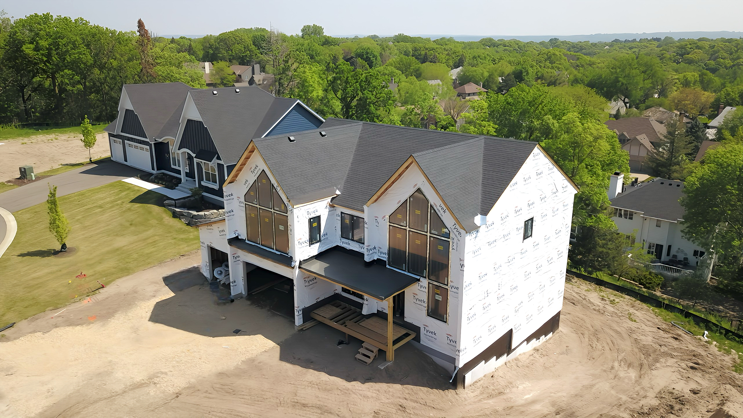 Aerial drone photo of new construction custom home exterior at framing stage with Tyvek housewrap, roofing complete, and large architectural window openings installed